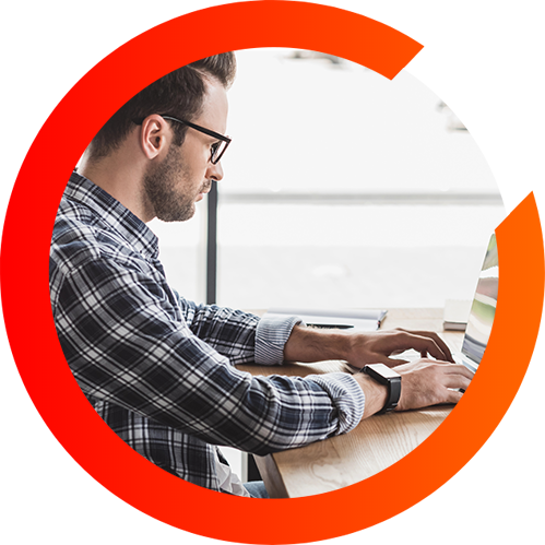 A man types on his laptop at his desk in a three quarter orange circle.